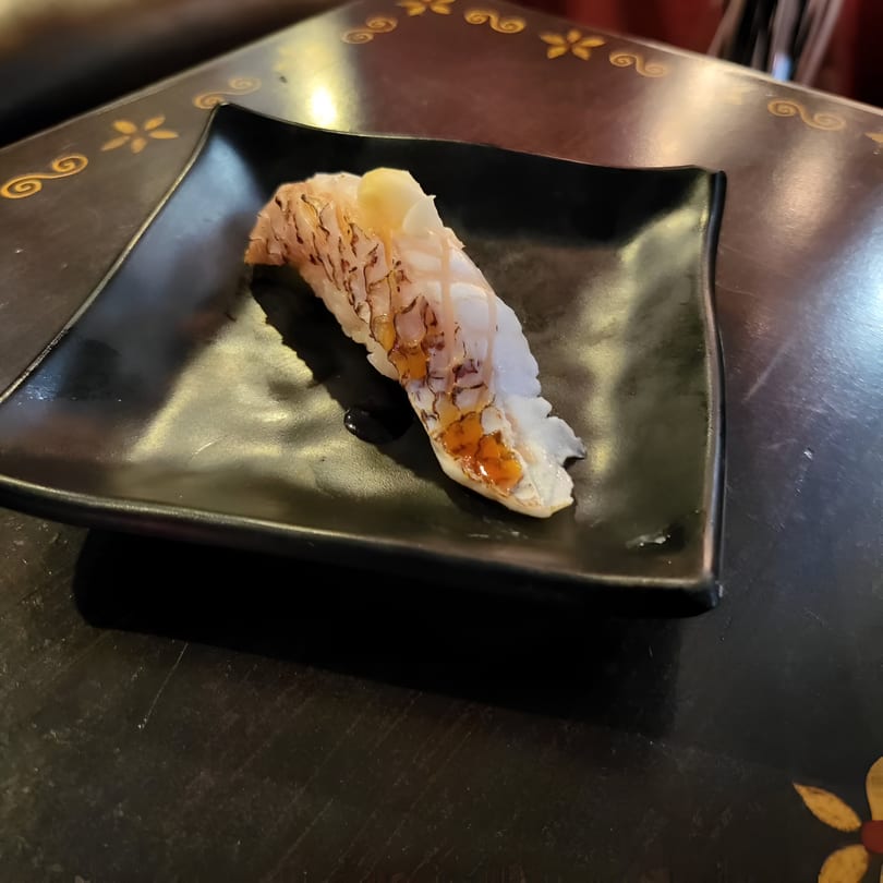 Miyozen's Japanese sushi, a piece of white fish nigiri with sauce on a black plate.